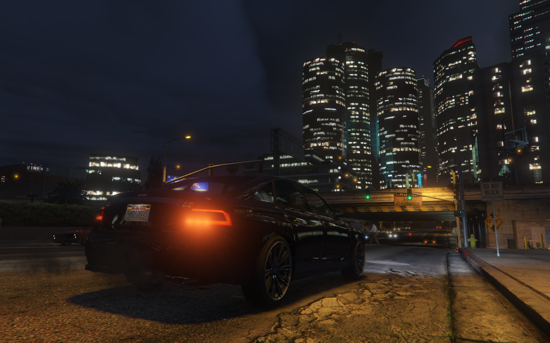 A black sports car drives towards high-rise buildings in GTA V's city of Los Santos.